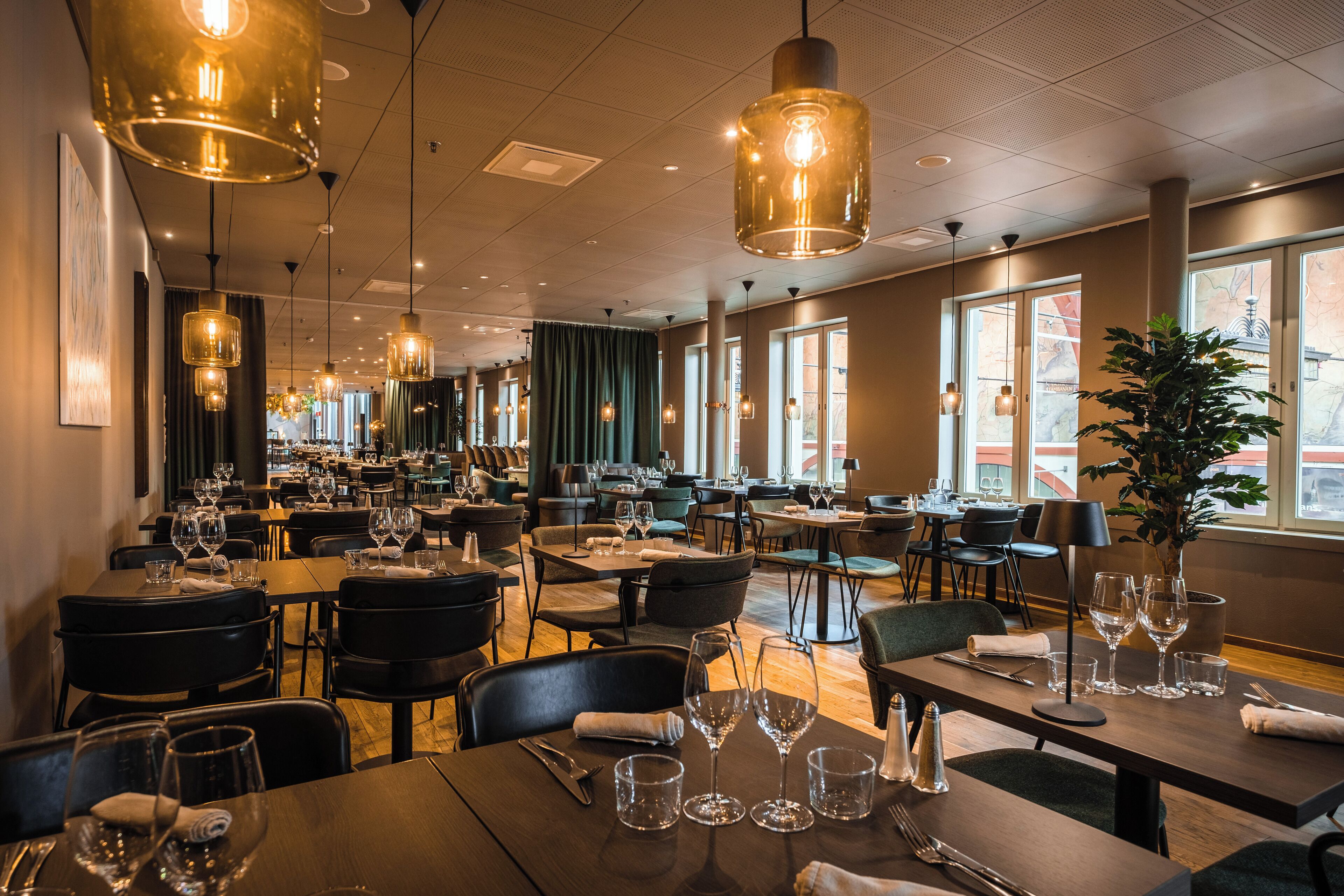 A restaurant with multiple dining tables, chairs, and hanging pendant lights.