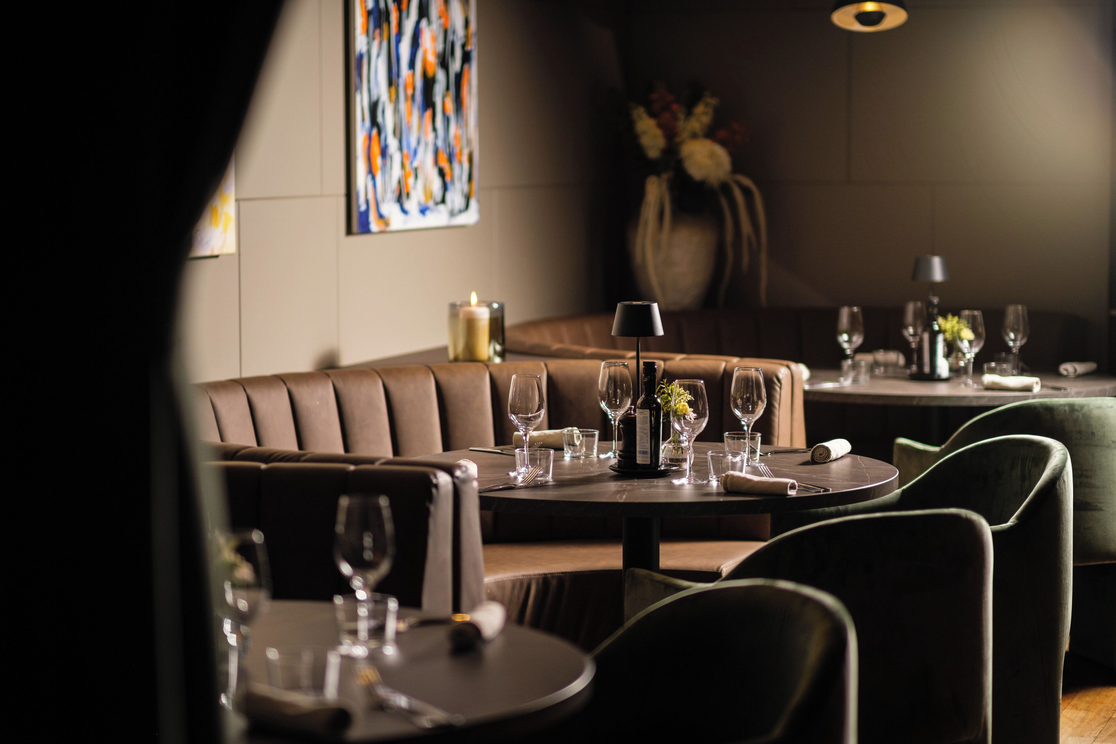 Un restaurante con zona de cabinas, mesas redondas y un florero con flores en la mesa.