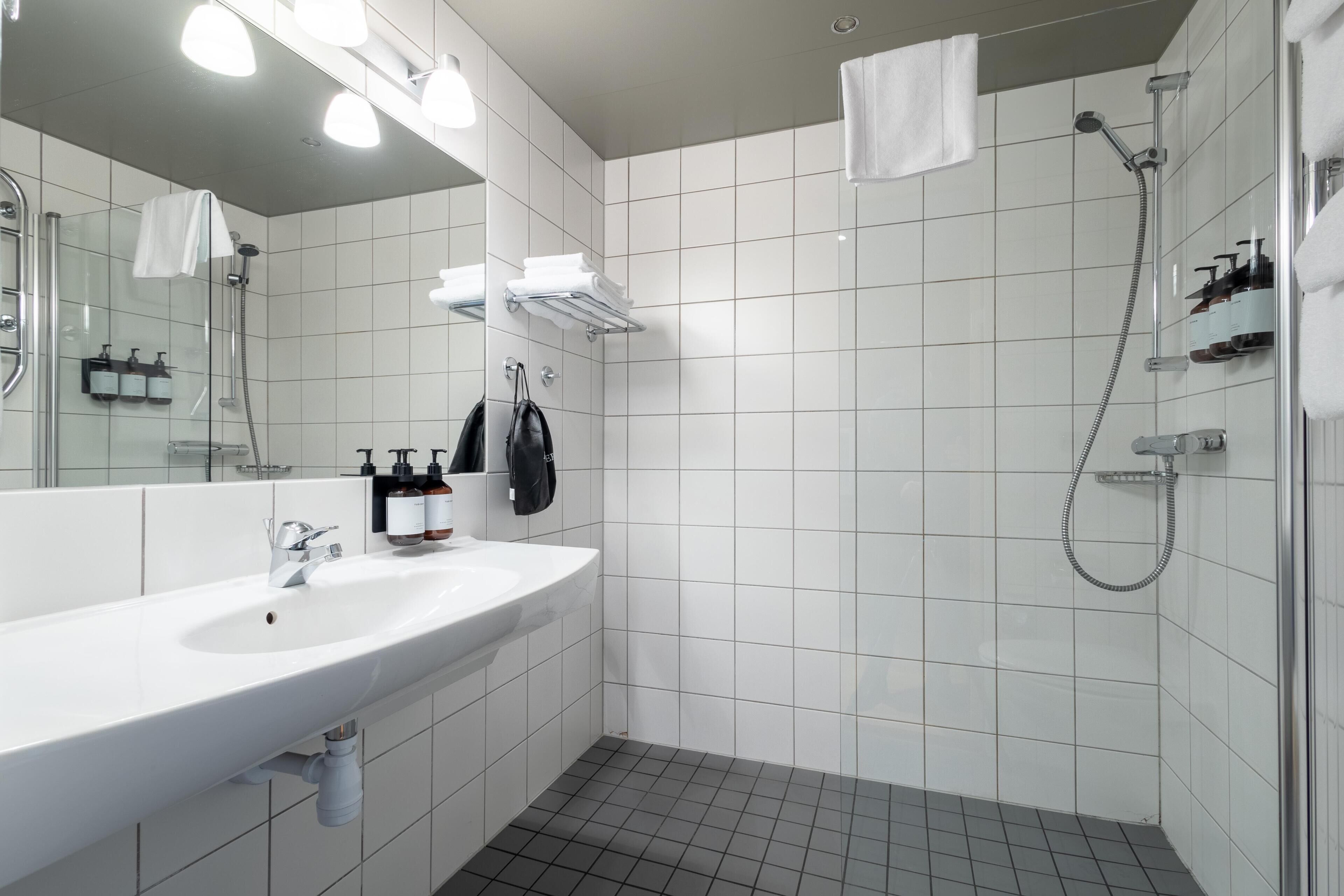 A modern bathroom with a white sink, mirror, and shower area.