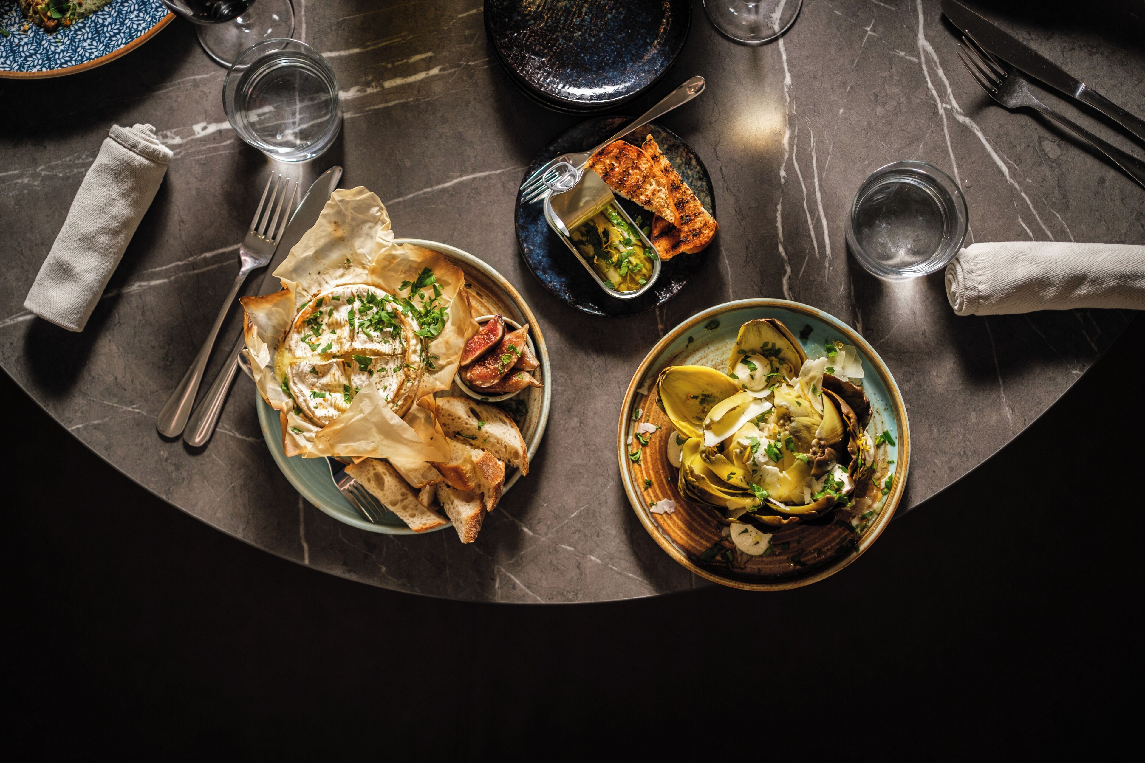Una mesa de comedor con platos de comida, cubiertos y vasos.
