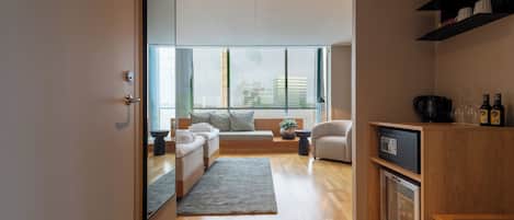 A modern living room with a sofa, a coffee table, and a rug. There is a kitchen area with a microwave and a cabinet.