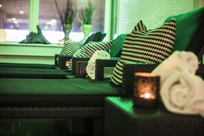 Een wellnessruimte met een groene bank, gekleurde kussens en een kaars.