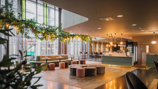 En modern hotellobby med en receptionsdisk, sittgrupper och stora fönster.