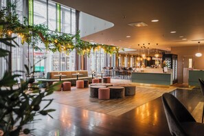 Un hall d’hôtel moderne avec un comptoir d’accueil, des espaces de détente et de grandes fenêtres.