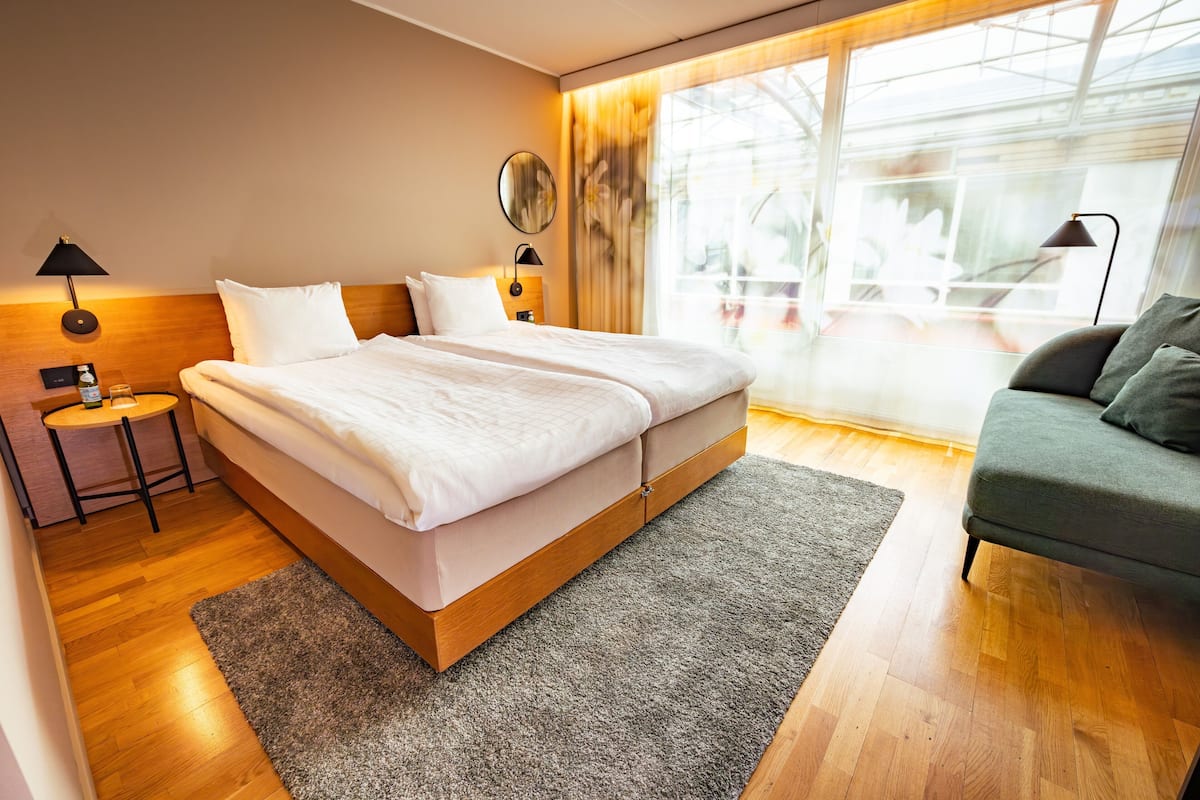 Ett modernt hotellrum med en stor säng, ett litet bord, en soffa och ett stort fönster med utsikt över omgivningarna.