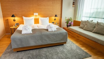 Una habitación de hotel con una cama grande, dos mesitas de noche con lámparas, un sofá y una ventana con cortinas.