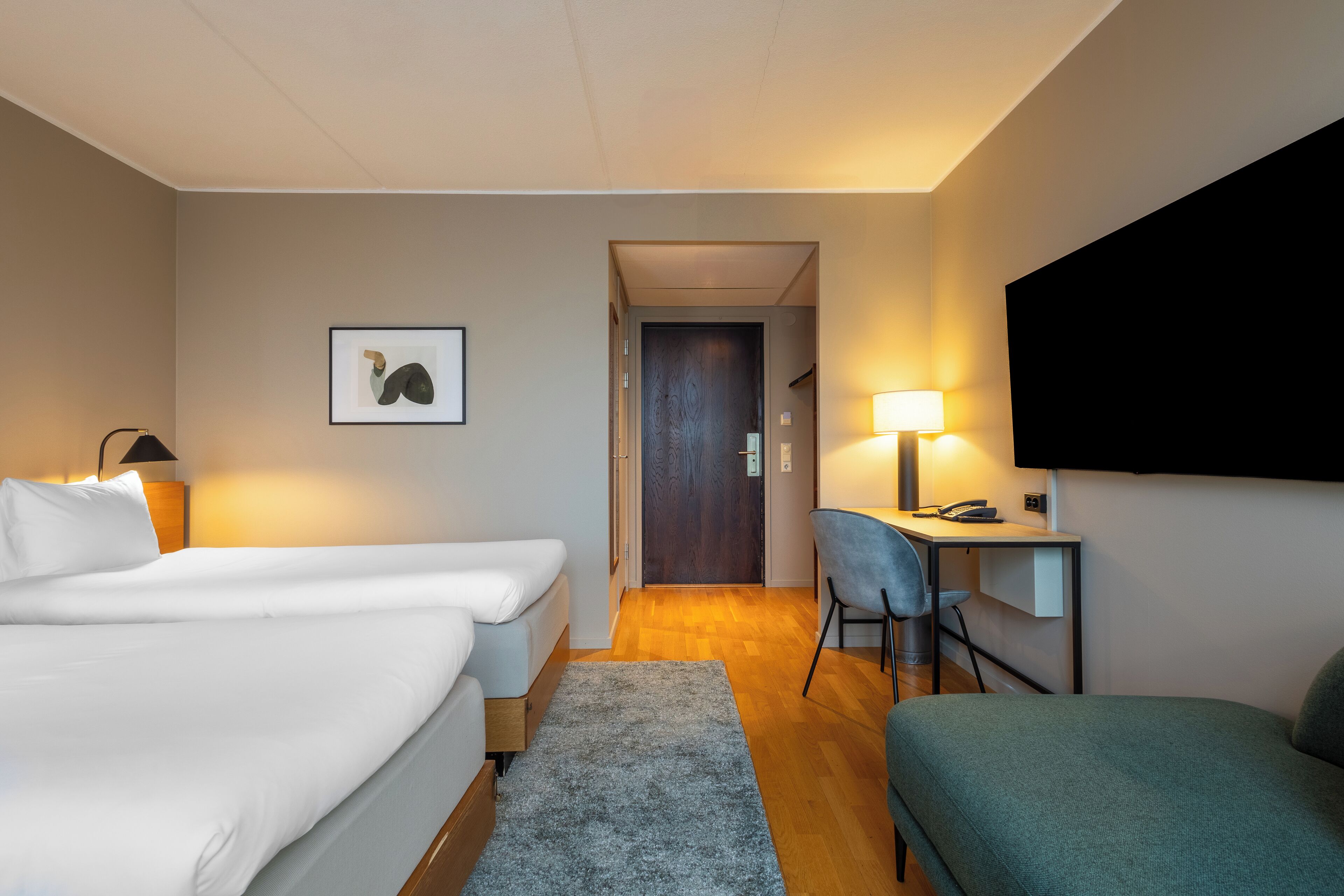 Una habitación de hotel con dos camas, un escritorio, una silla, un televisor y un cuadro en la pared.