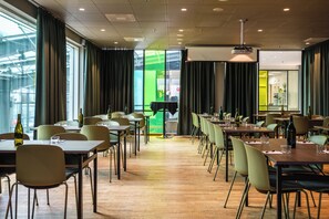 Un espace de restauration moderne, doté de tables et de chaises, de grandes fenêtres et d’un mur d’accent vert.