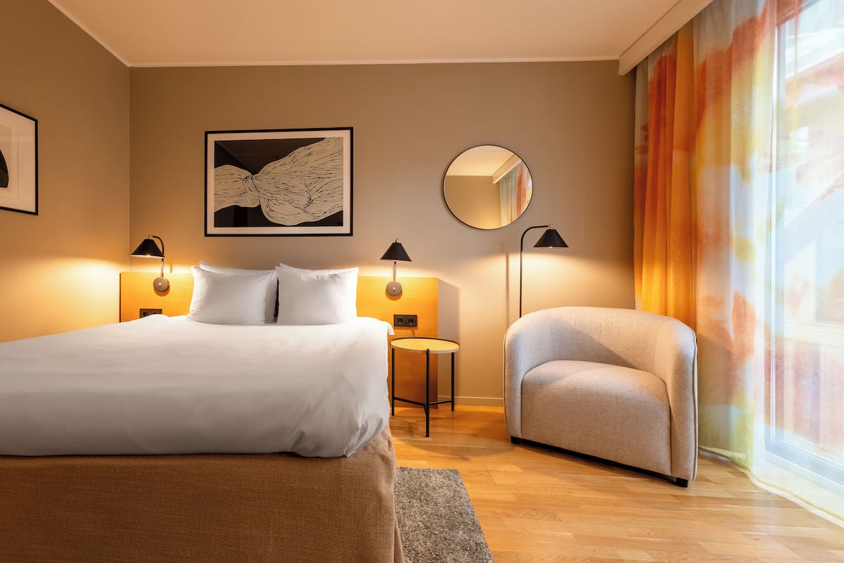 Ett hotellrum med en säng, en stol, en rund spegel och två vägglampor.
