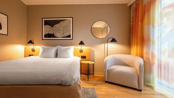 A hotel room with a bed, a chair, a round mirror, and two wall-mounted lamps.