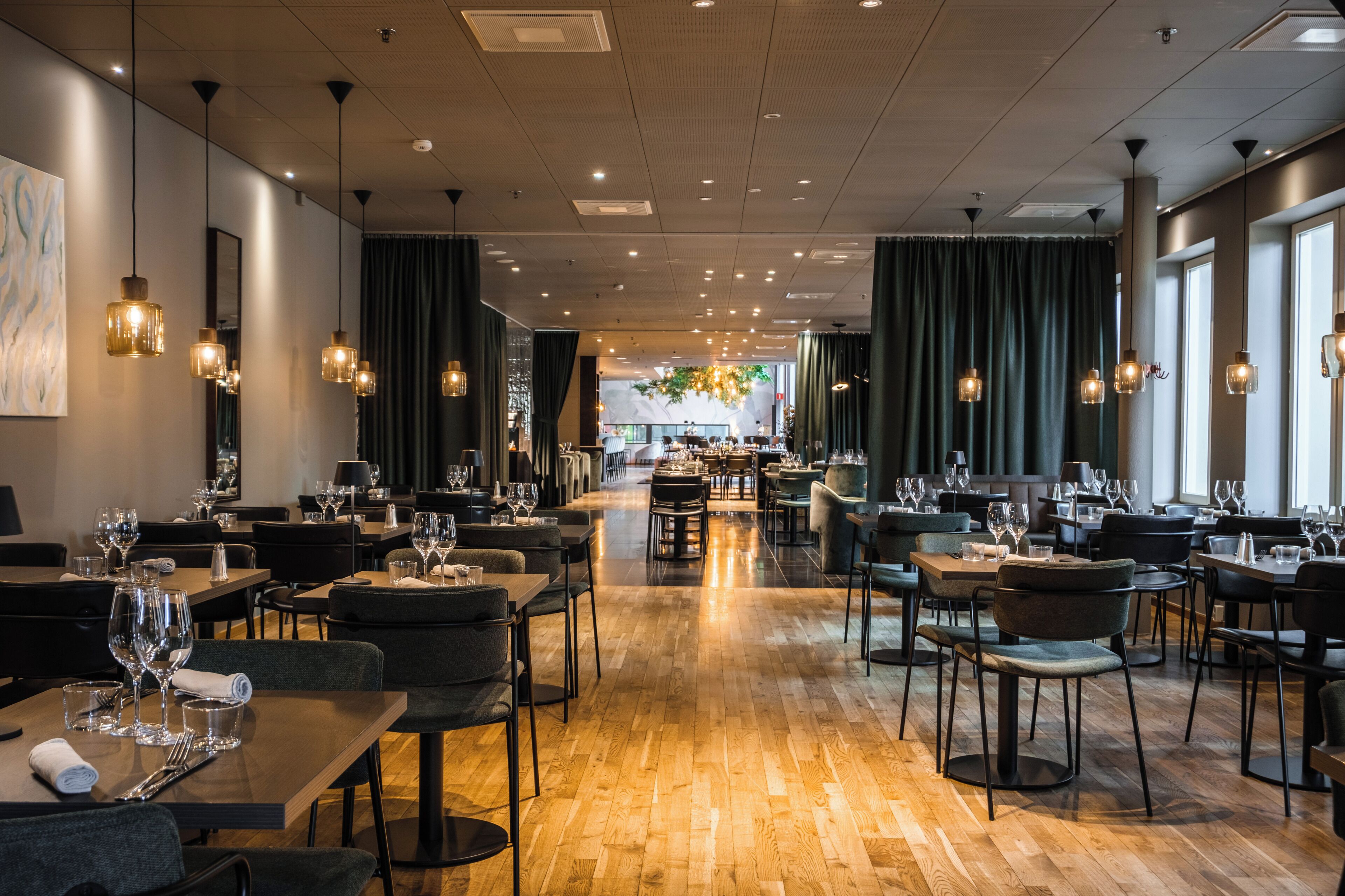 Un restaurante amplio con suelo de madera, varias mesas de comedor y lámparas colgantes.