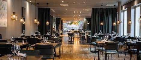 Un restaurante amplio con suelo de madera, varias mesas de comedor y lámparas colgantes.