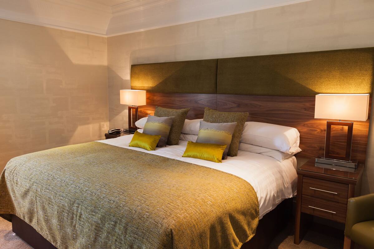 Una habitación de hotel con una cama grande, dos mesitas de noche y un tocador.