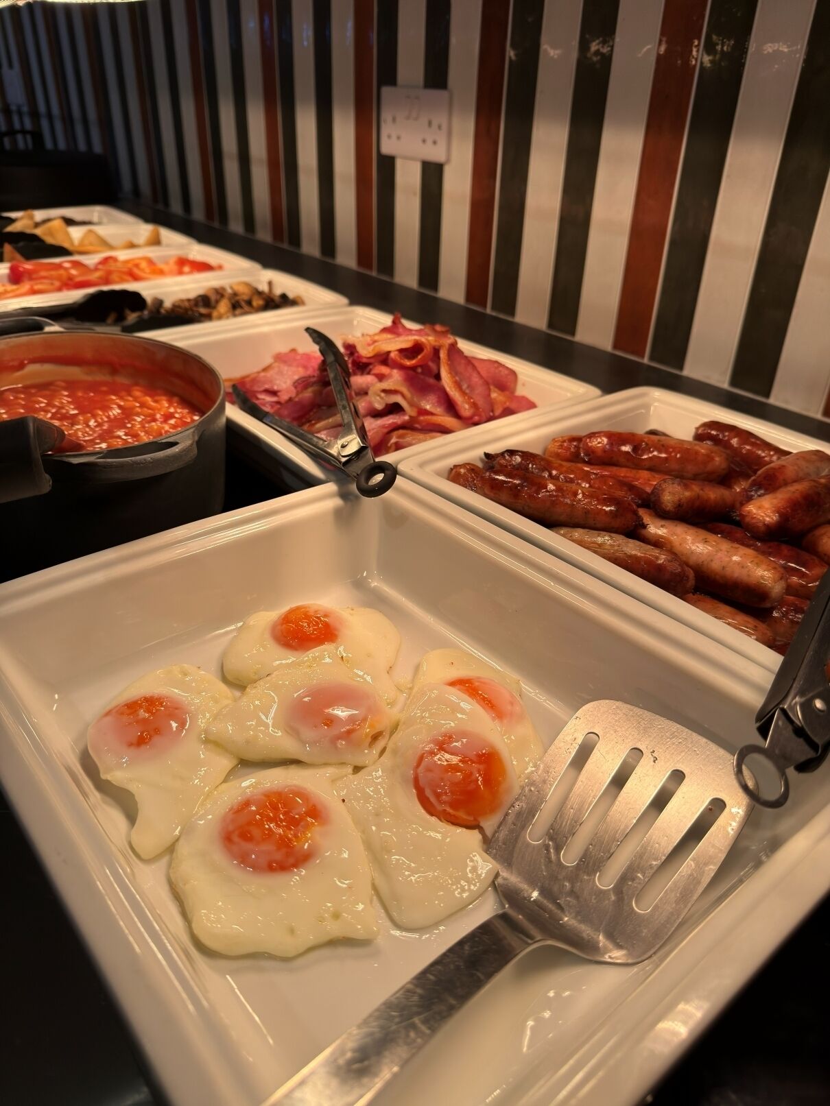 Een buffet met diverse gerechtjes, waaronder eieren, worstjes en een soepketel.
