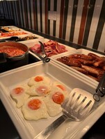 Un bufé con diversas opciones de comida, incluyendo huevos, salchichas y una olla de sopa.