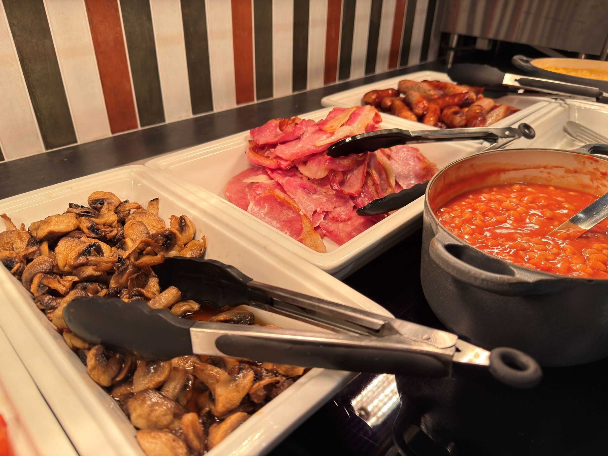 A buffet with various dishes including mushrooms, bacon, and baked beans.