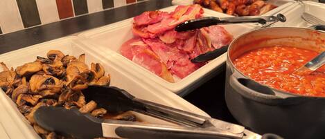 A buffet with various dishes including mushrooms, bacon, and baked beans.