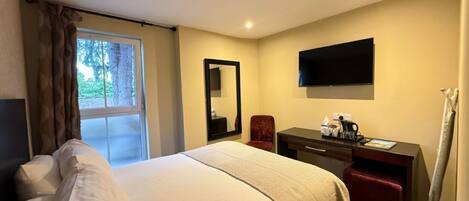 A hotel room with a bed, a desk, a chair, a TV, and a window with curtains.