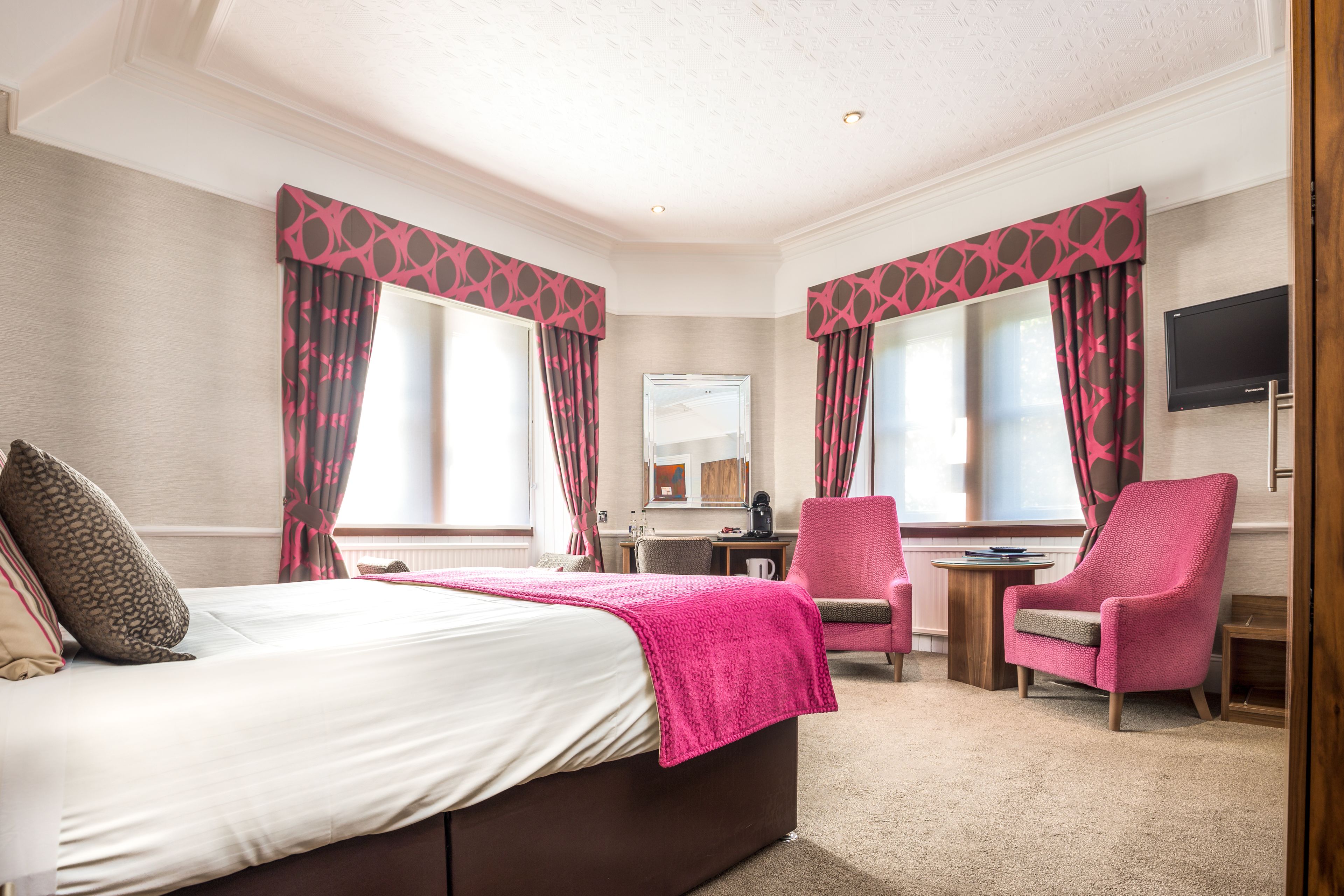 A hotel room with a bed, two armchairs, a desk, and a TV.
