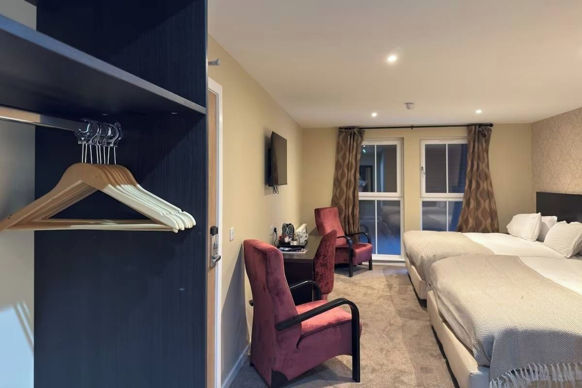 A hotel room with a bed, a desk, a chair, a TV, and a coat rack.