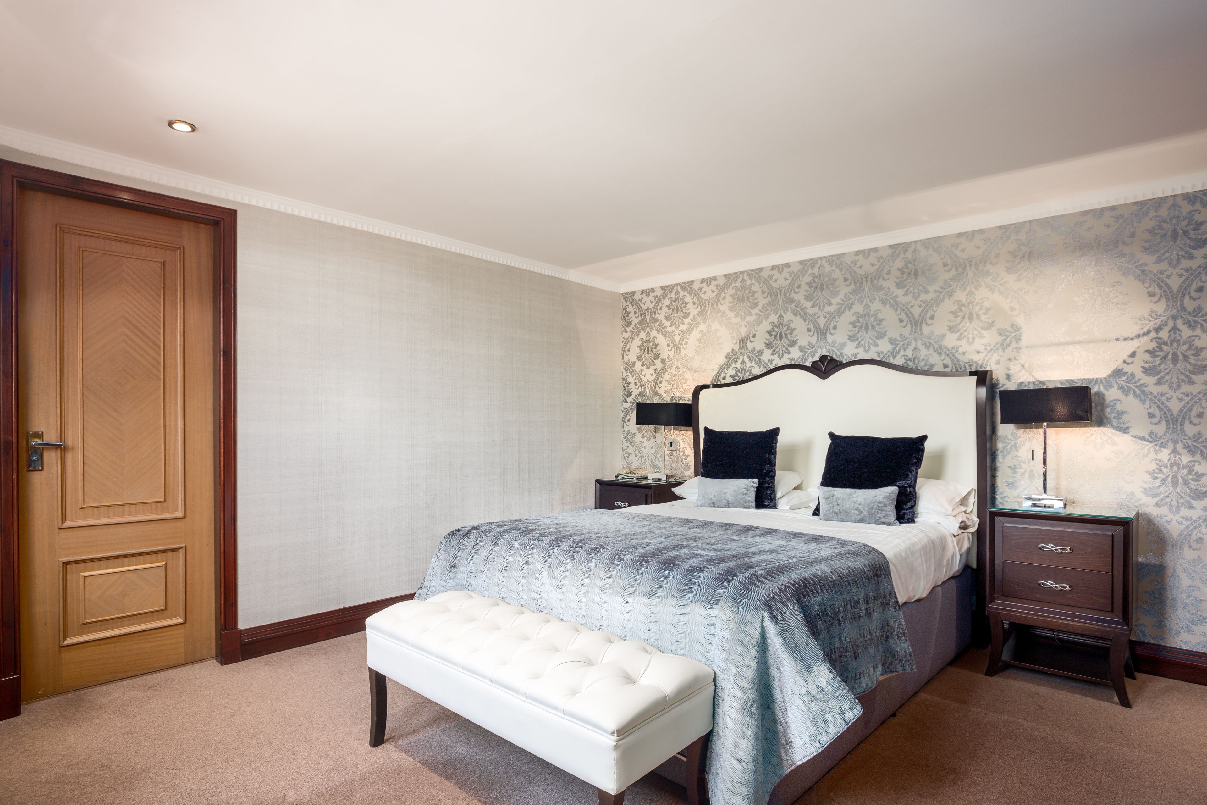 A bedroom with a large bed, a bedside table, a bench, and a wardrobe.