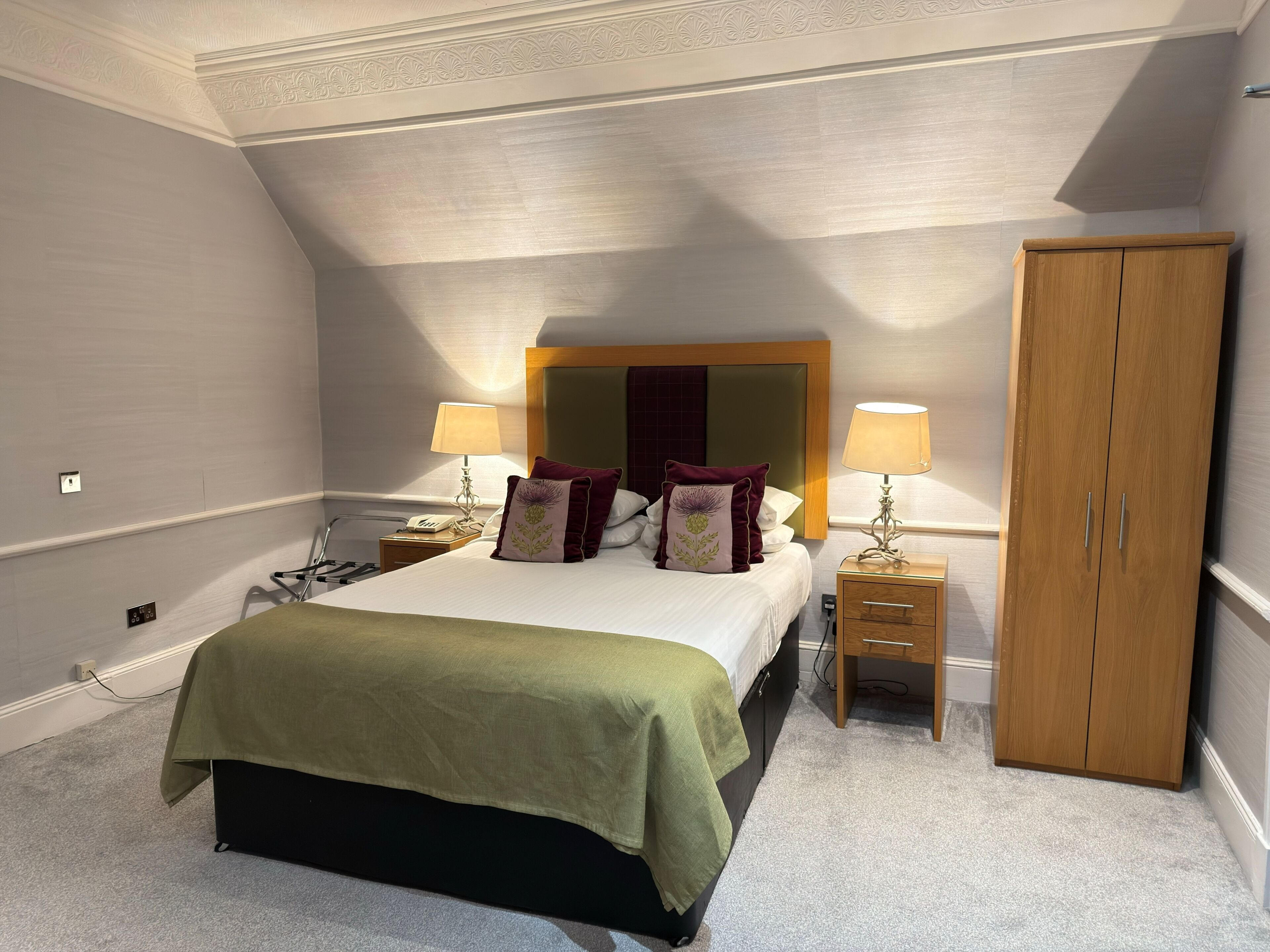 A bedroom with a bed, two bedside tables, a wardrobe, and a ceiling with a decorative pattern.