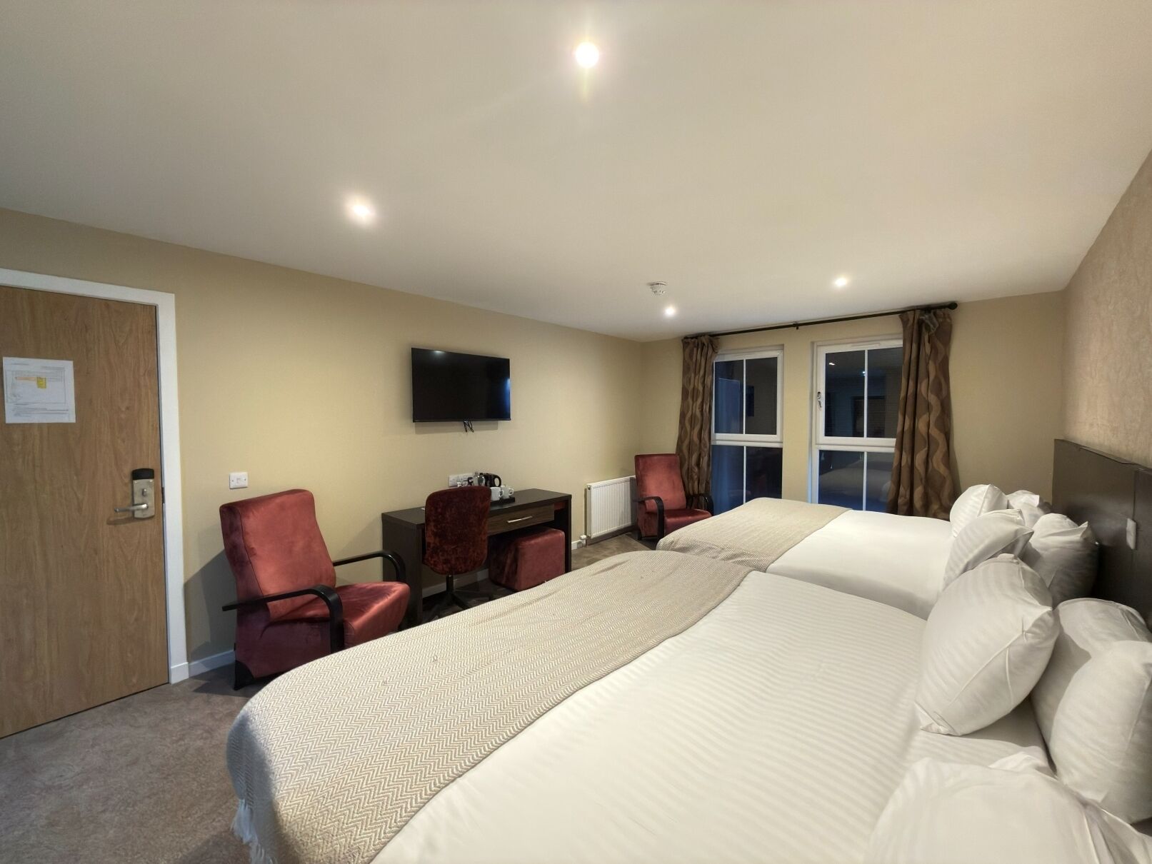 A hotel room with a bed, two chairs, a desk, a television, and a window with curtains.