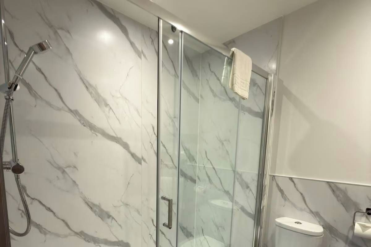 A modern bathroom with a glass-enclosed shower, marble walls, and a white sink.