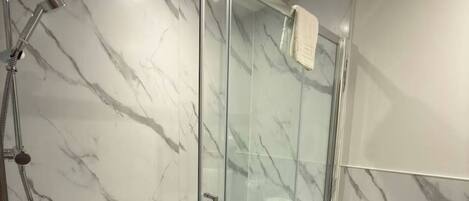 A modern bathroom with a glass-enclosed shower, marble walls, and a white sink.