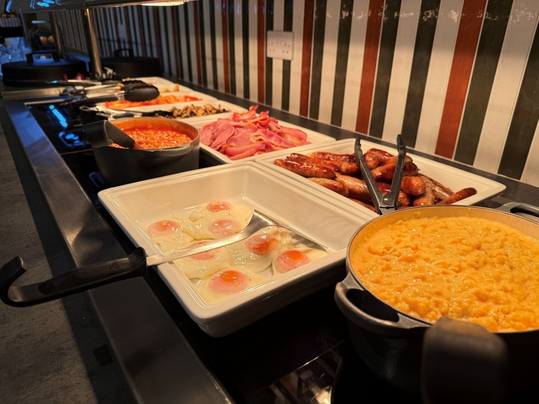 A buffet with various food items including eggs, sausages, and a pot of soup.