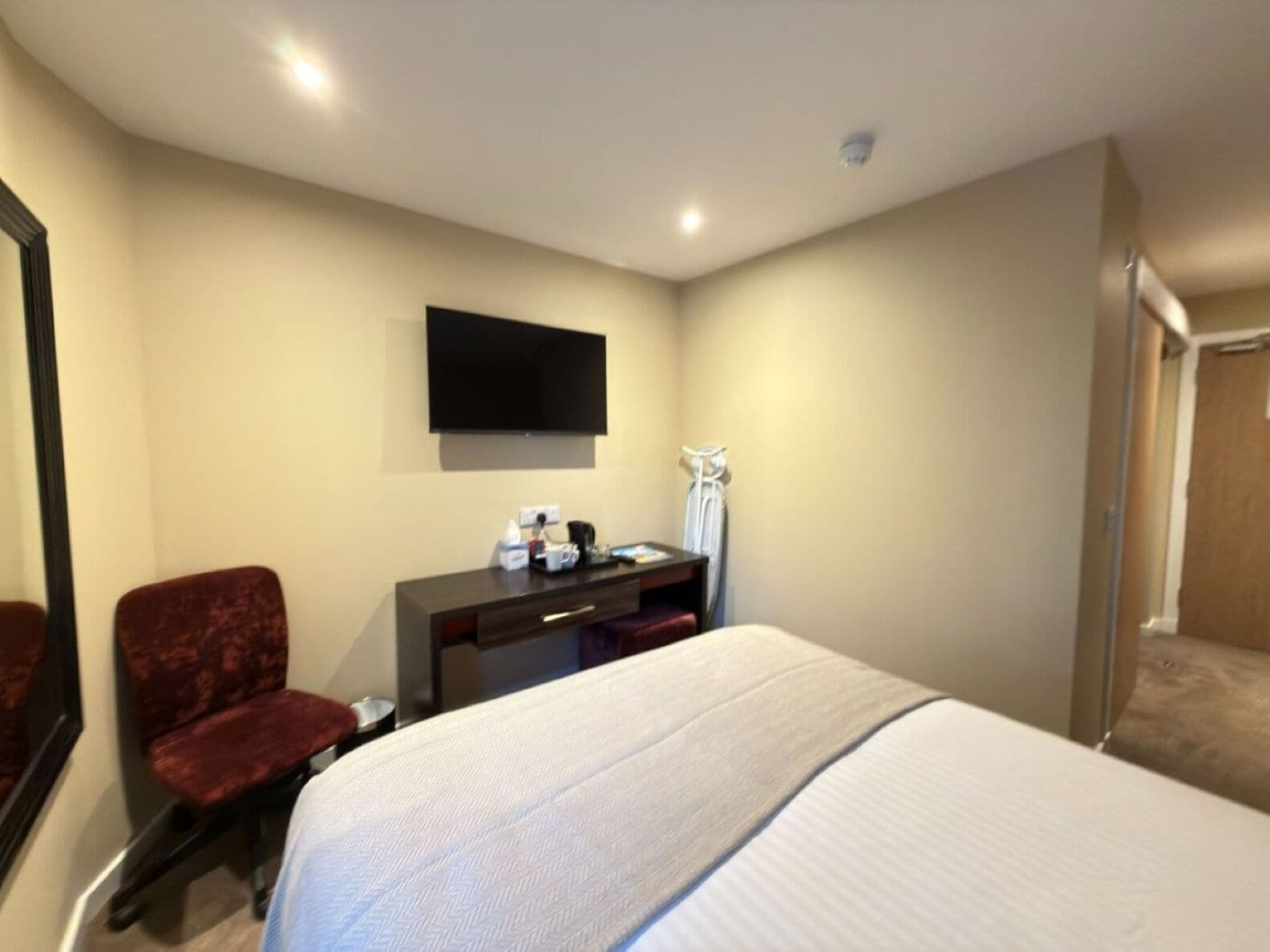 A hotel room with a bed, a desk, a chair, a flat-screen TV, and a mirror.