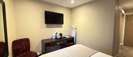 A hotel room with a bed, a desk, a chair, a flat-screen TV, and a mirror.