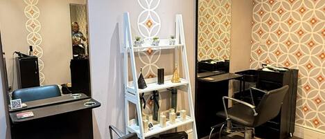 Un salón con espejo, sillas, una estantería con productos y papel tapiz estampado.