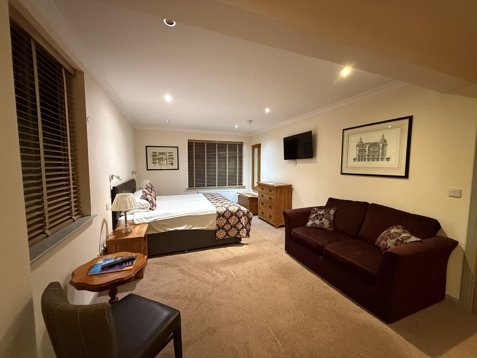 A bedroom with a bed, bedside table, lamp, dresser, and a TV on the wall.