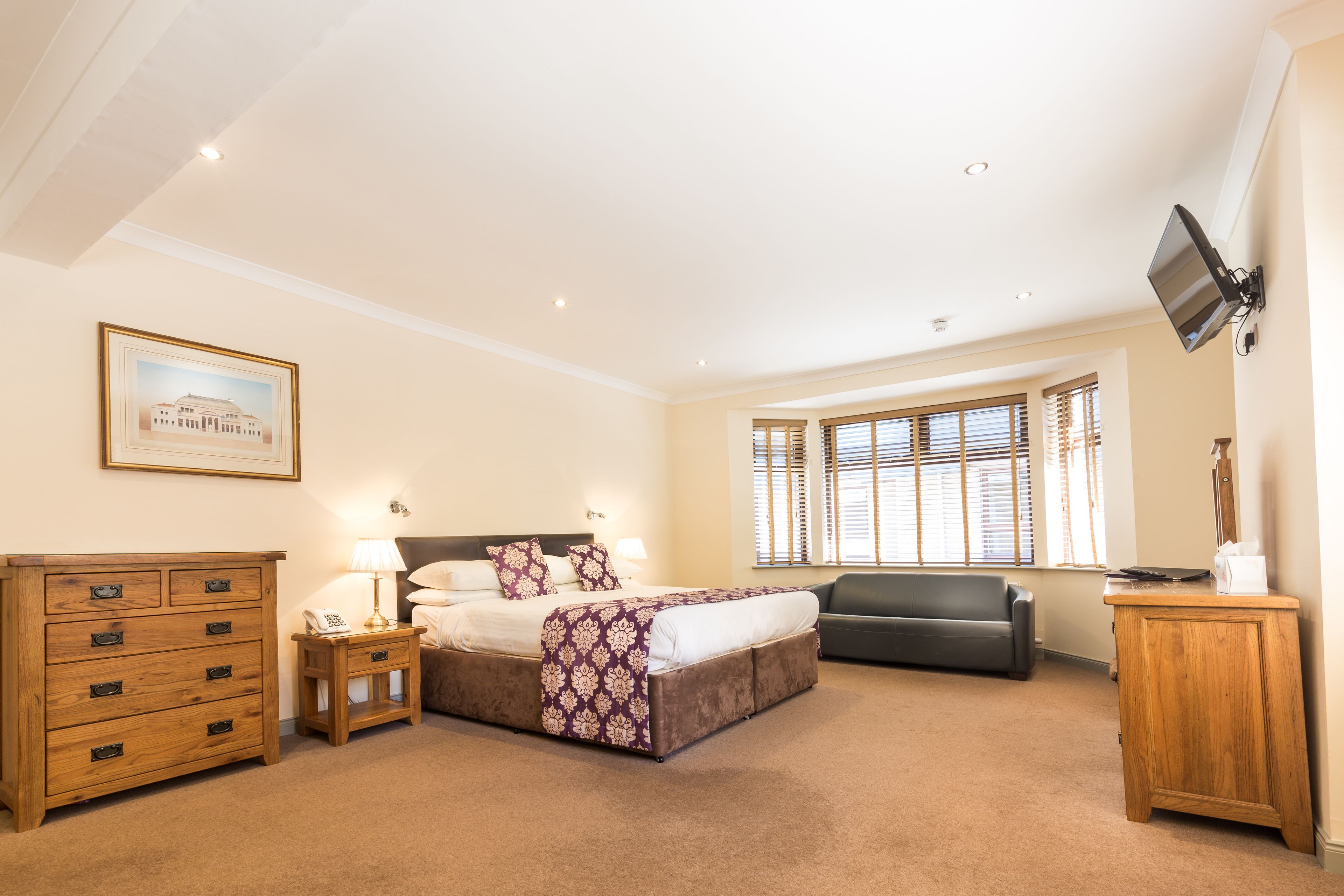 A bedroom with a bed, bedside tables, a dresser, a television, and a window with blinds.