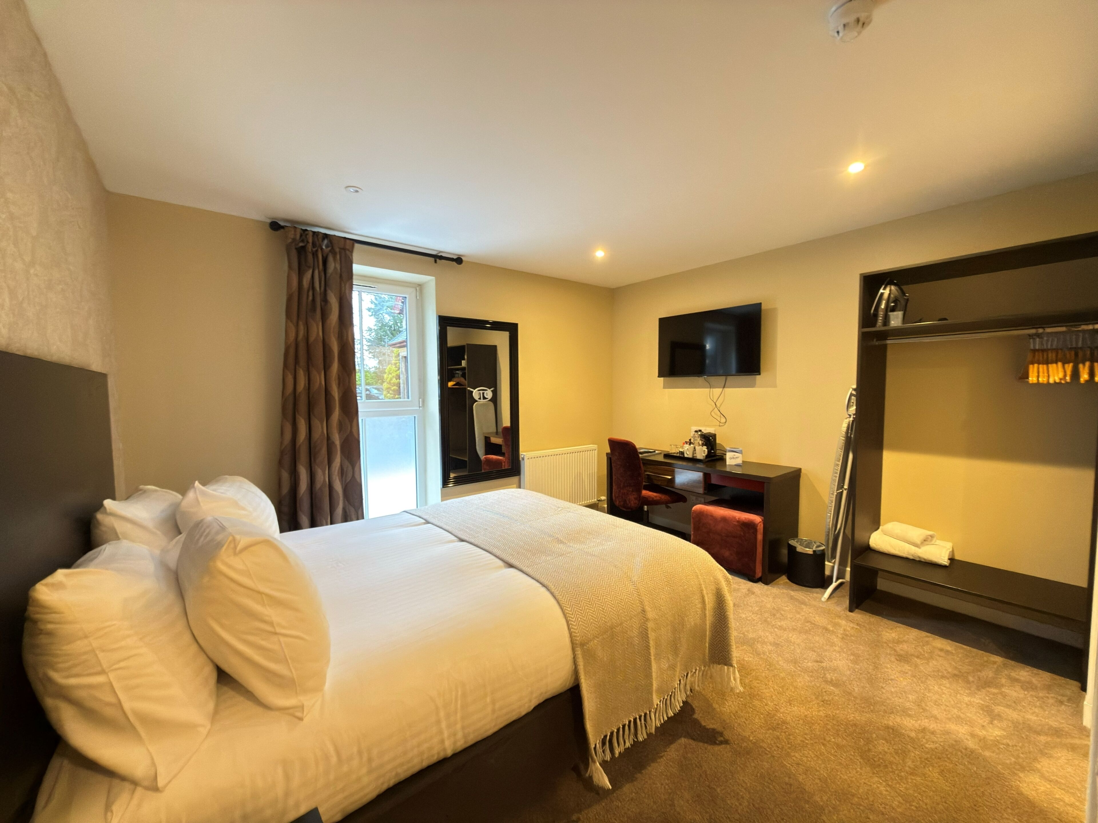 Ein Hotelzimmer mit Bett, Schreibtisch, Sessel, Fernseher und Kleiderschrank.