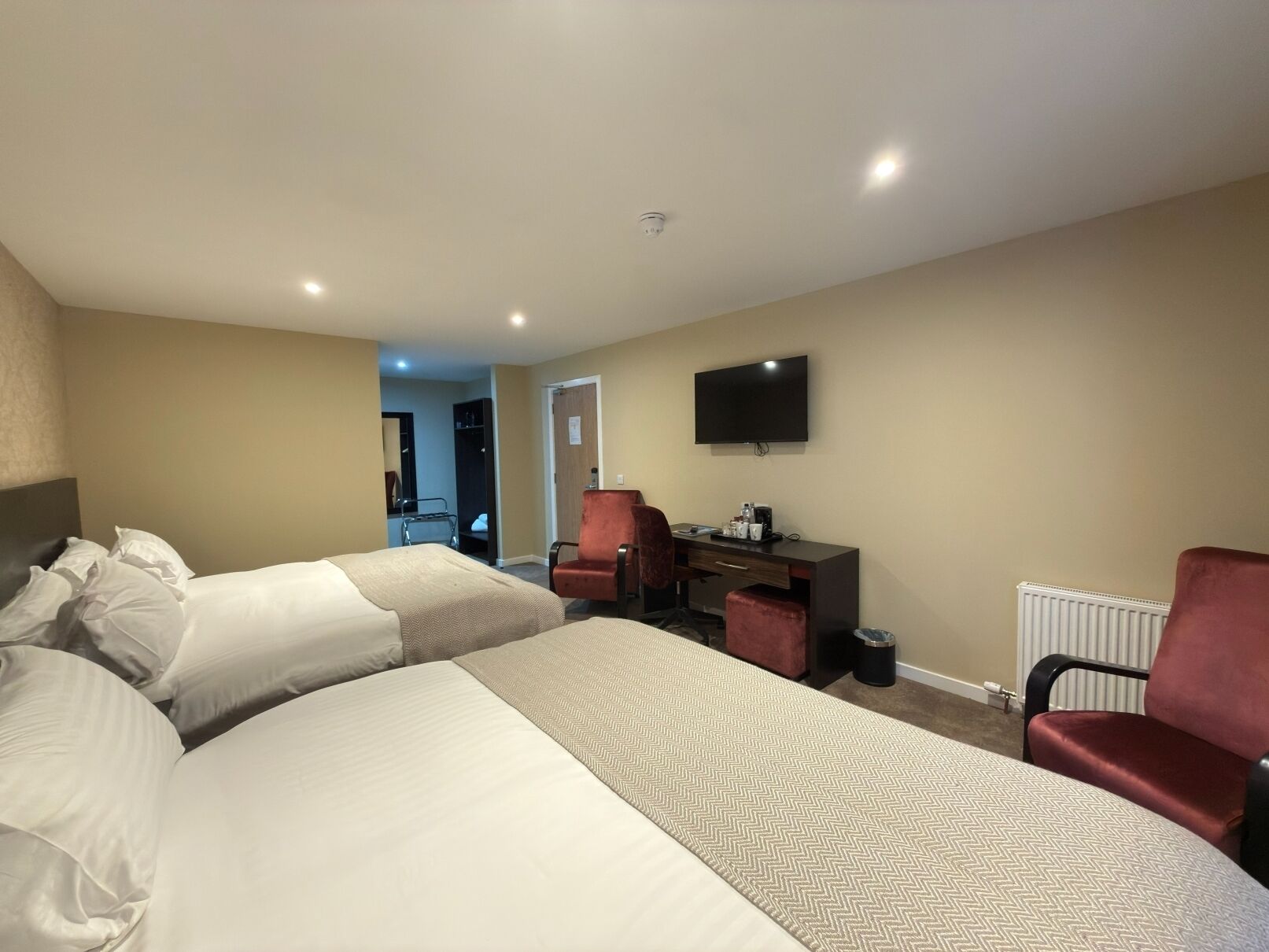 A hotel room with two beds, a desk, a chair, a television, and a radiator.