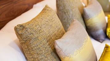 A close-up of a bed with a white sheet and several pillows in various shades of yellow and beige.