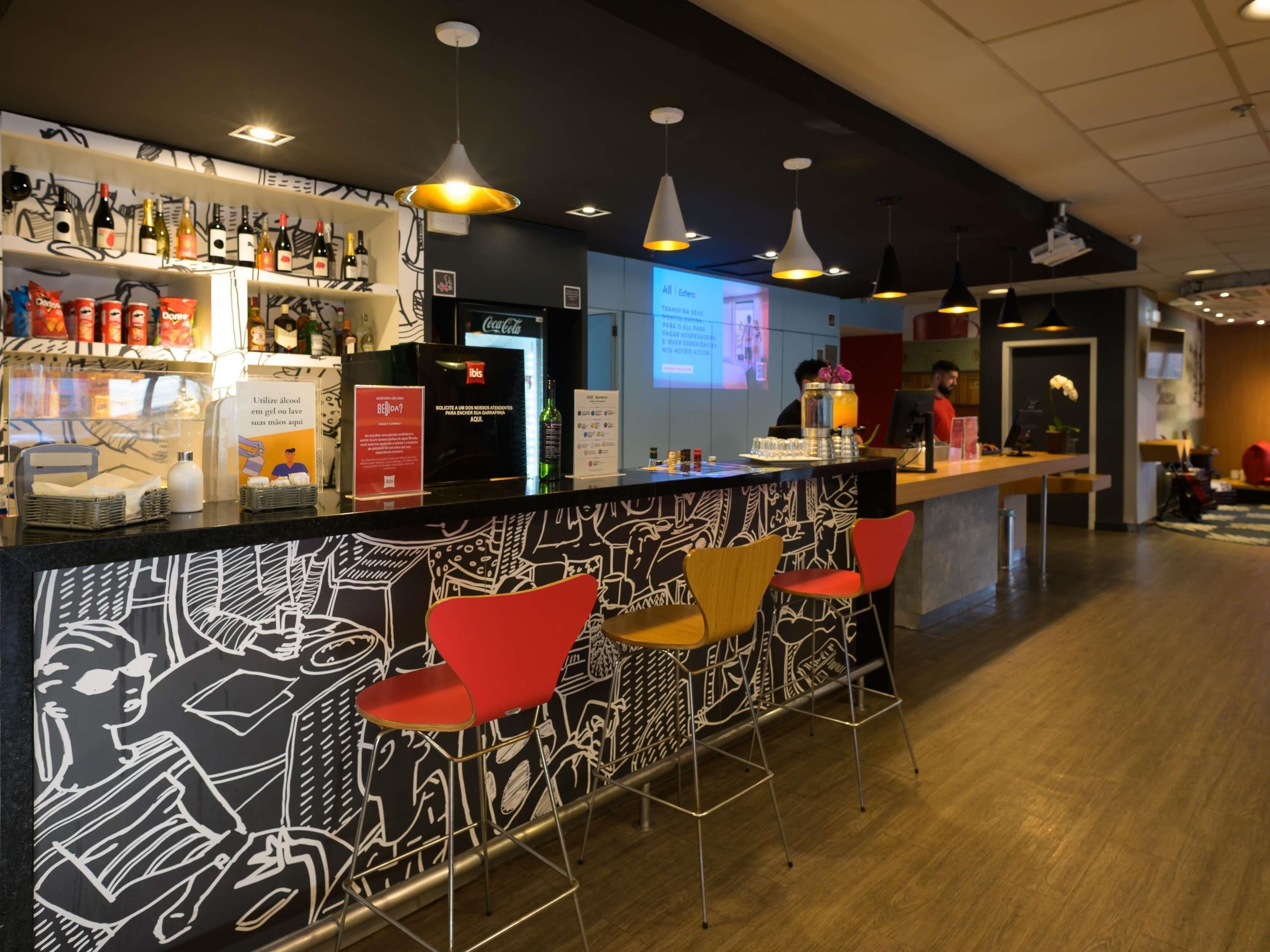 Un espace bar avec un comptoir, des étagères remplies de bouteilles et des chaises rouges.