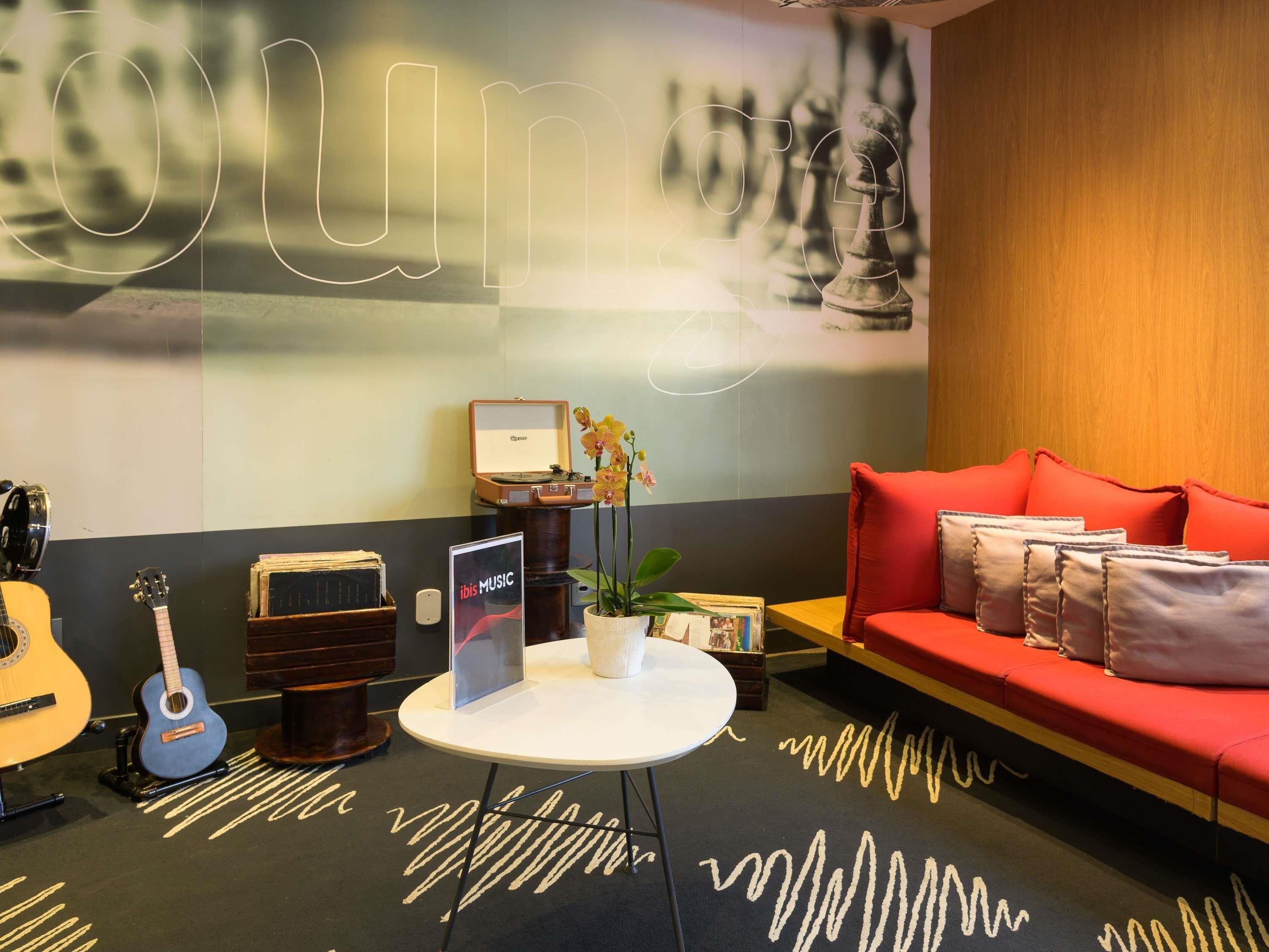 A room with a red sofa, a white table, a guitar, a record player, and a wall with abstract art.