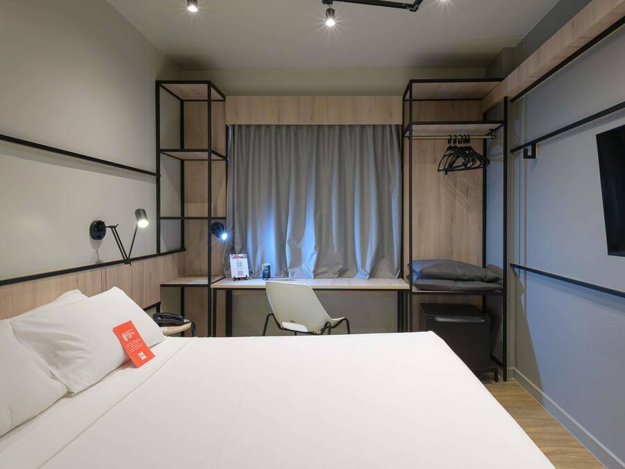 Una habitación de hotel moderna con cama, escritorio, silla y armario con ropa colgada.