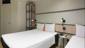 Et hotelværelse med en stor seng, et natbord med lampe, telefon og en lille hylde med en flaske.