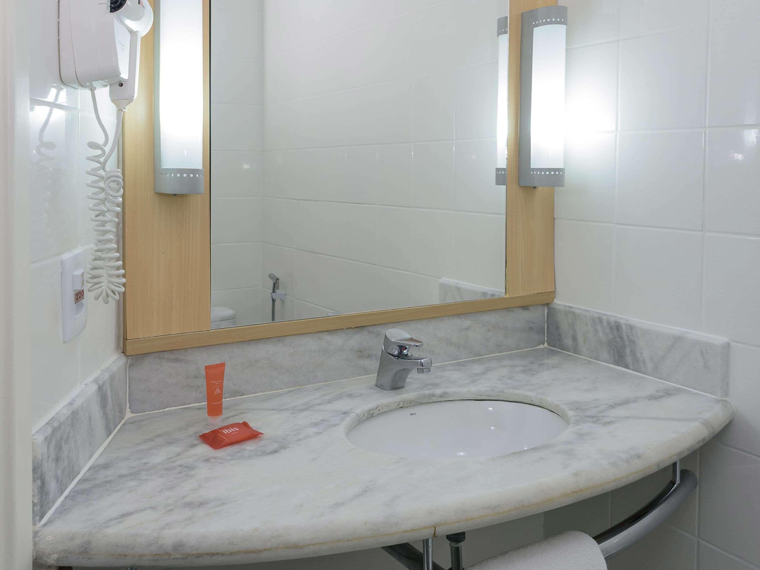 A bathroom with a marble sink, a mirror, a handheld hair dryer, and a towel rack.