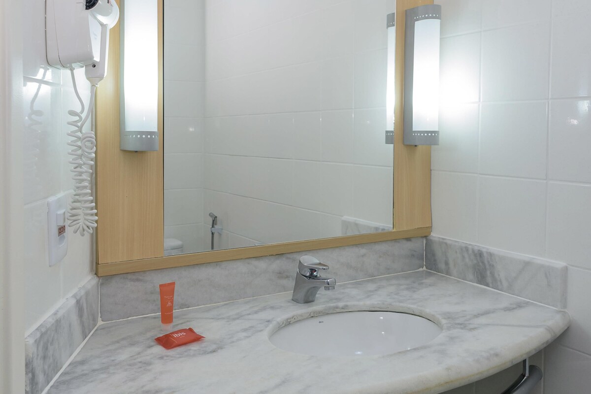 A bathroom with a marble sink, a mirror, a handheld hair dryer, and a towel rack.