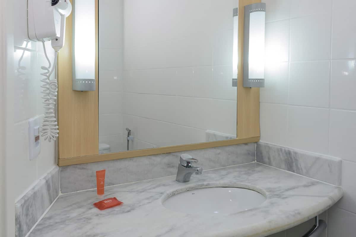 A bathroom with a marble sink, a mirror, a handheld hair dryer, and a towel rack.
