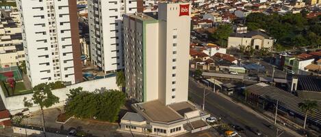 A high-rise building with a prominent red and white logo, surrounded by a dense urban area with various buildings and a busy street.