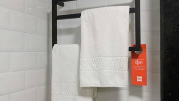 Un baño con paredes de azulejos blancos, un toallero negro que sostiene dos toallas blancas y una etiqueta naranja con texto.