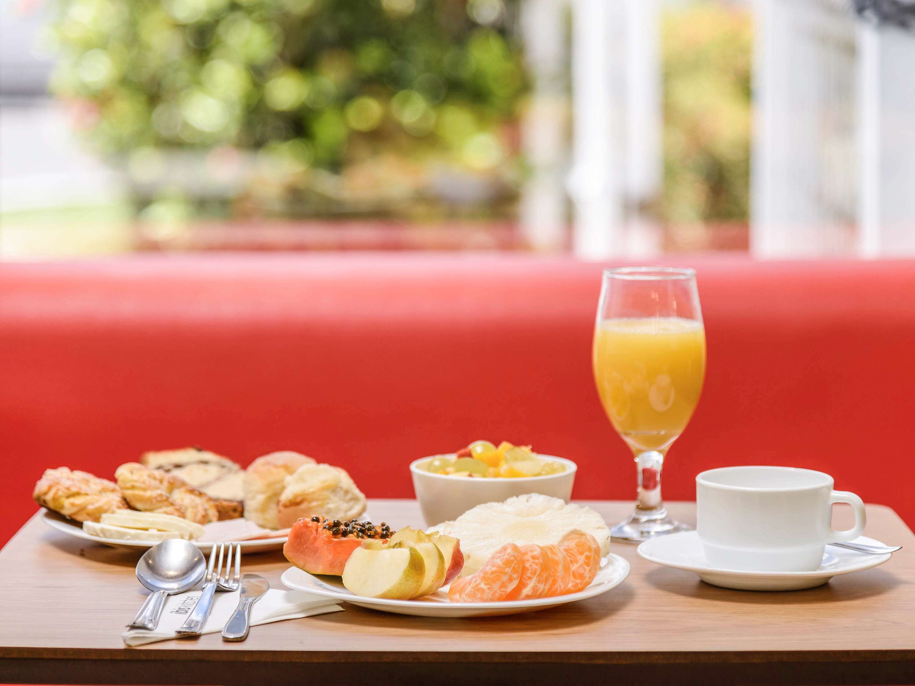 Una mesa de desayuno con pasteles, fruta, un vaso de zumo de naranja y una taza de café.