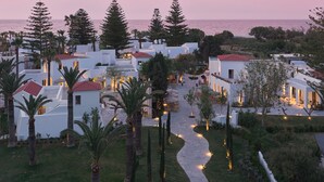 Un complejo turístico costero con edificios blancos, palmeras y un paseo empedrado que conduce al mar.