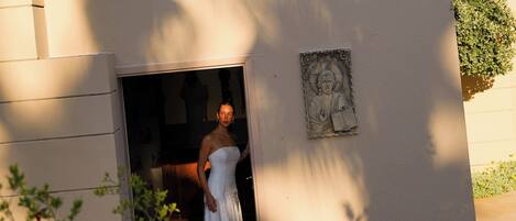 A person in a white dress standing at the entrance of a building with a stone relief on the wall.
